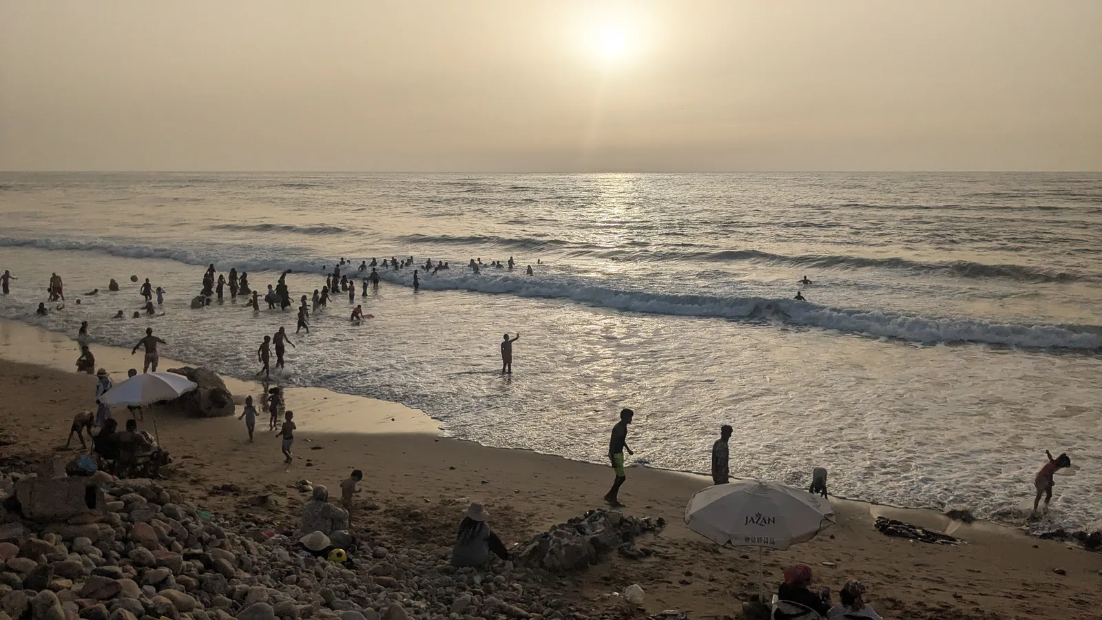 People swimming and walking on Sidi Ifni beach at sunset