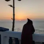 Person in traditional clothing watching the Atlantic sunset from the Sidi Ifni corniche