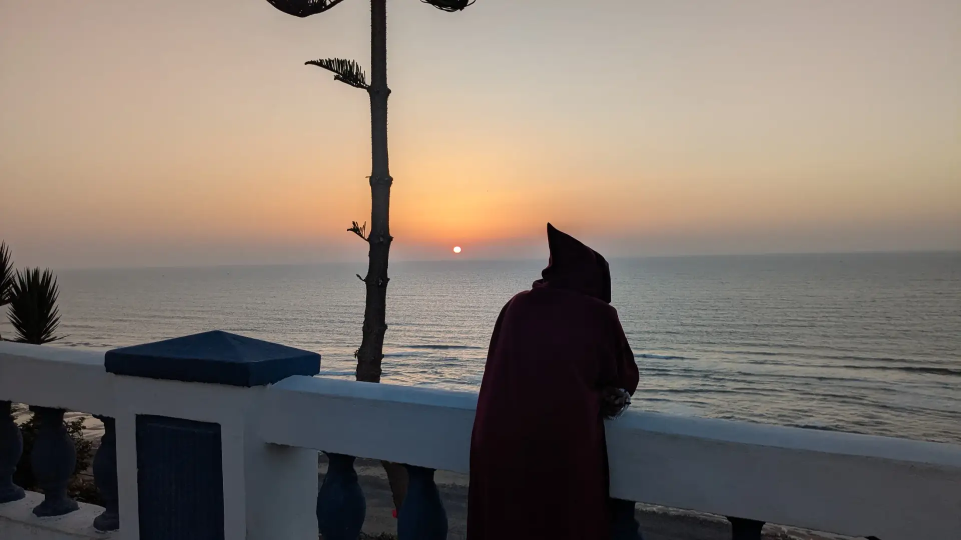 Person in traditional clothing watching the Atlantic sunset from the Sidi Ifni corniche